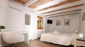 Un dormitori amb llit, escriptori, cadira, televisió i obra d'art a les parets.