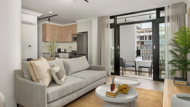 Ein modernes Wohnzimmer mit grauem Sofa, einem Couchtisch und Blick auf Küche und Balkon.