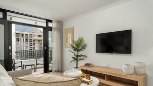 Ein modernes Wohnzimmer mit großem Fernseher, einem Blumentopf und einem Balkon mit Blick auf die Stadt.