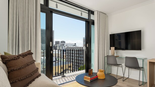A modern living room with a sofa, a coffee table, and a TV mounted on the wall. - The York | Designer CBD Apartment (Cape Town)