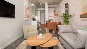 A modern living room with a sofa, armchair, and coffee table. There is a dining area with chairs and a table in the background. - Coastal Studio in the Heart of Sea Point | Pool (Cape Town)
