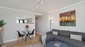 Un salon moderne avec un canapé gris, une table basse, un coin repas comprenant une table et des chaises, et un tableau accroché au mur.