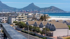 Un paysage urbain côtier avec des bâtiments modernes, une plage et une montagne imposante en arrière-plan.