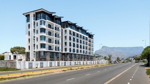 Un hôtel moderne à plusieurs étages, doté d’une entrée imposante, de grandes fenêtres et offrant une vue sur les montagnes en arrière-plan.