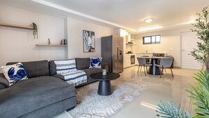 Ein modernes Wohnzimmer mit einem grauen Sofa, einem runden schwarzen Couchtisch und einem Essbereich mit kleinem Tisch und Stühlen.