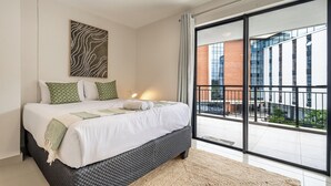 Ein modernes Schlafzimmer mit einem großen Bett, Blick auf ein Gebäude durch eine Glasdoor und einem an der Wand befestigten abstrakten Kunstwerk.