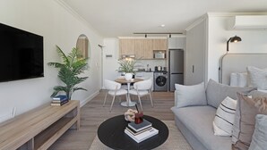 Ein modernes Wohnzimmer mit einem schwarzen Couchtisch, einer Couch, einem Fernseher, einem Essbereich mit Tisch und Stühlen sowie einer Küche im Hintergrund.