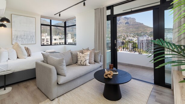 Ein modernes Wohnzimmer mit einer Couch, einem Couchtisch und Blick auf eine Stadtlandschaft durch große Fenster.