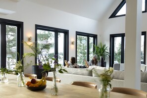 Una sala de estar moderna con ventanas amplias, una mesa de comedor con fruta y un sofá.