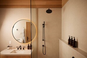 Un baño moderno con un espejo redondo, un lavabo, una ducha y un estante con artículos de aseo.