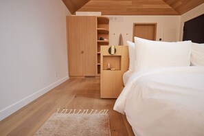 Un dormitorio con un armario de madera, una mesita de noche y una cama con ropa de cama blanca.