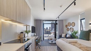 A modern hotel room with a kitchenette, a bed, a desk, and a balcony with a city view. - Cosy Studio Apartment | The York (Cape Town)