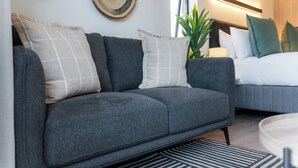 A modern living room with a grey sofa, a striped rug, and a bed with white bedding. - Cosy Studio Apartment | The York (Cape Town)
