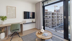 A modern living room with a large window, a flat-screen TV, a desk, and a comfortable chair. - Cosy Studio Apartment | The York (Cape Town)