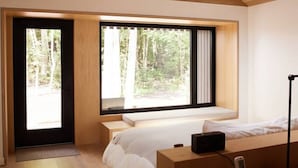 Een moderne slaapkamer met een groot bed, een bureau en uitzicht op een bos door de ramen.