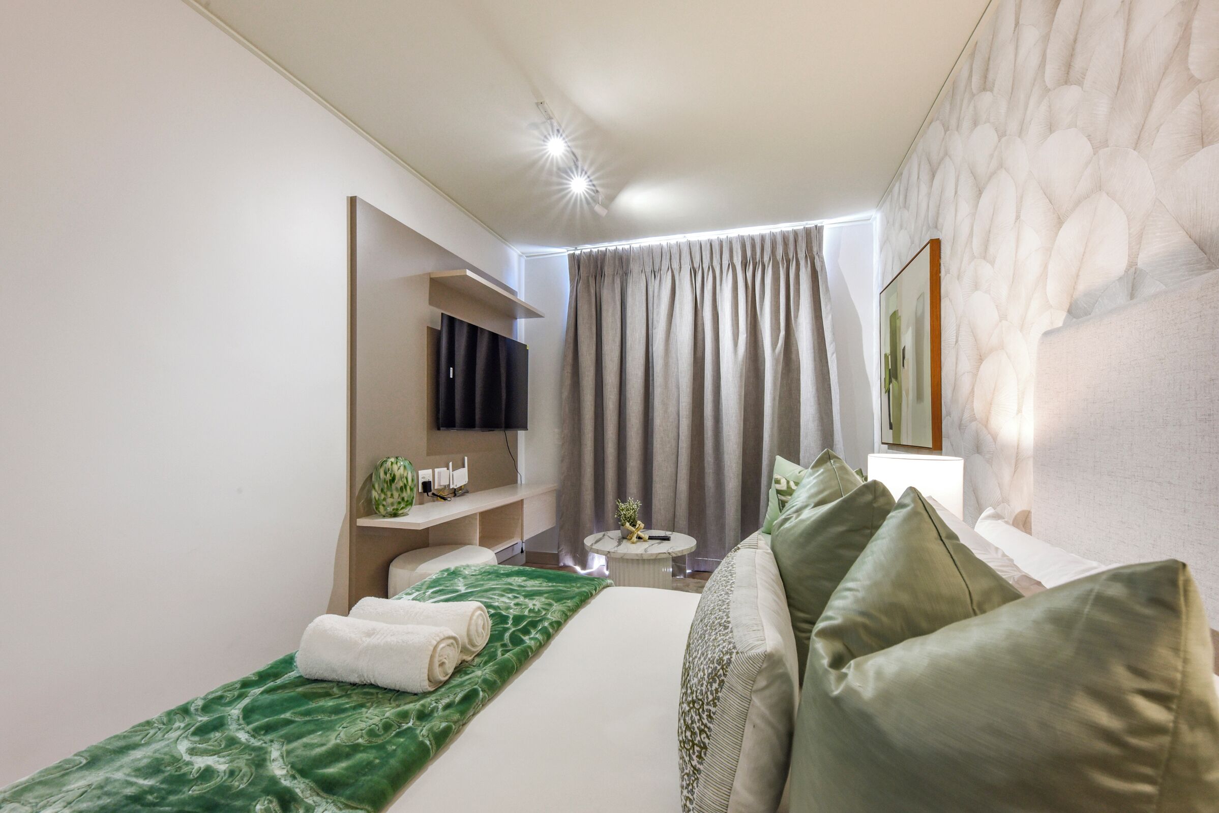 Habitació d'hotel moderna amb un llit, una petita zona de seients, un televisor i un quadre a la paret.