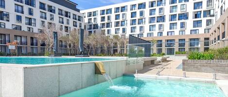 Un hotel moderno con piscina, varios balcones y cielo despejado.