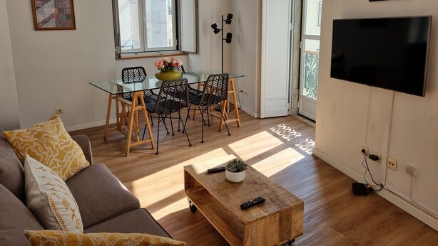 Ein modernes Wohnzimmer mit einem Glastisch, schwarzen Stühlen, einem Holztisch und einem an der Wand montierten Flachbildfernseher.
