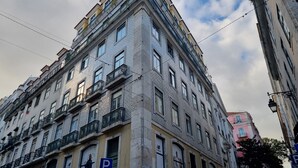 Ein mehrstöckiges Gebäude mit Hauseingang an der Ecke, mehreren Balkonen und einem sichtbaren Parkplatzschild.