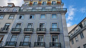 Ein mehrstöckiges Gebäude mit einem gemusterten Fassadenschmuck, Balkonen mit Metallgeländern und einem strahlend blauen Himmel im Hintergrund.