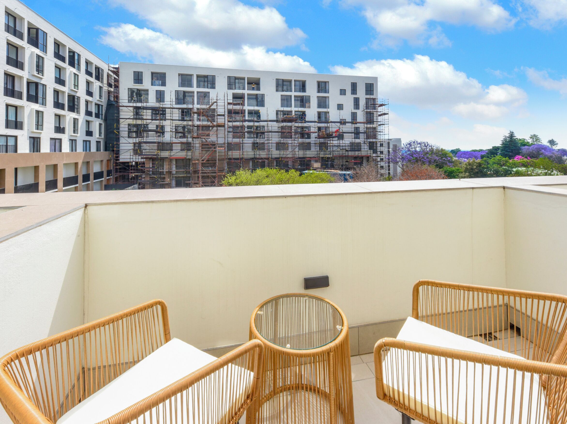 A rooftop terrace with wicker chairs and a table, overlooking a building under construction with scaffolding.