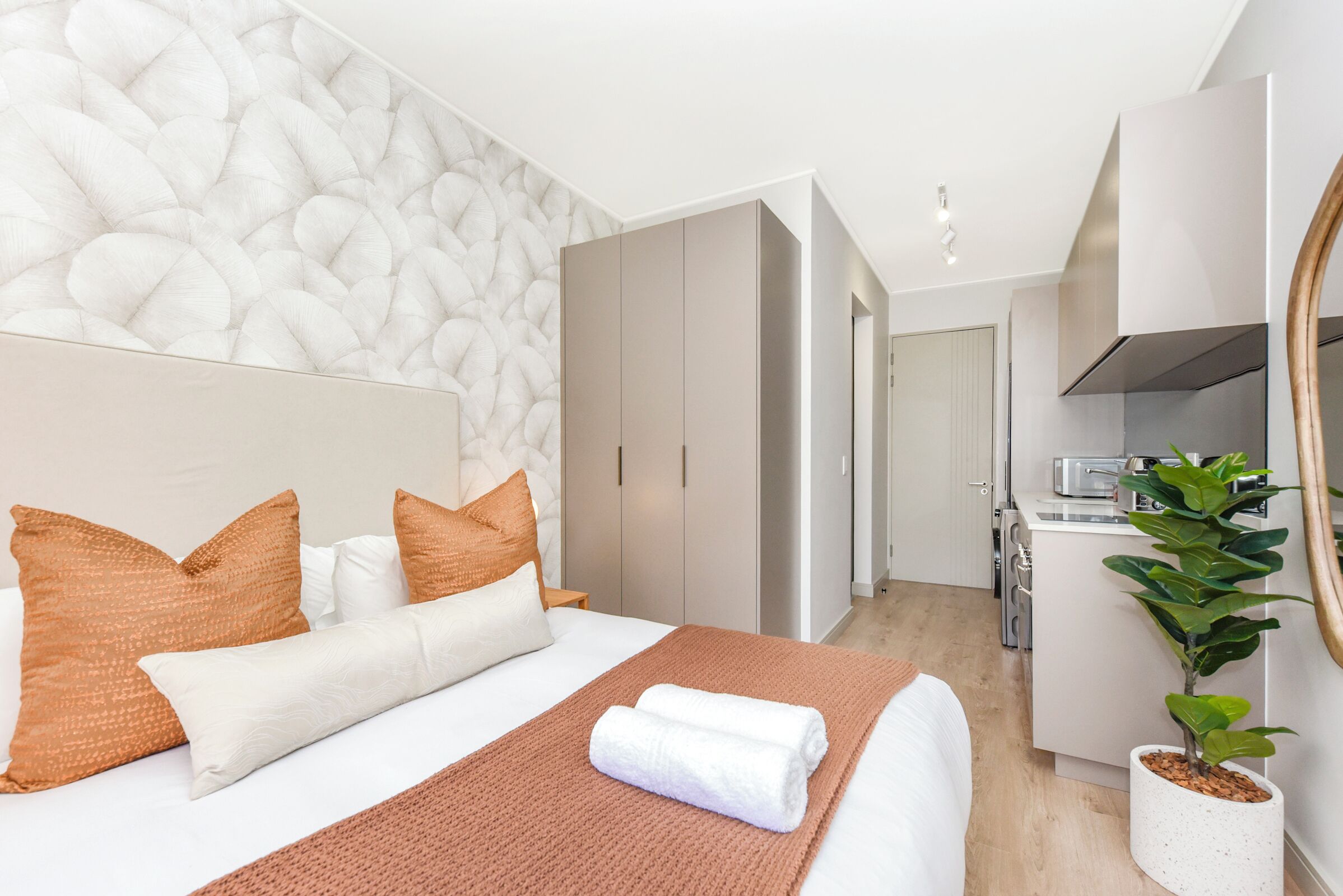 Una habitación de hotel moderna con una cama grande, una zona de cocina y una planta en maceta.