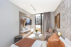 Quarto de hotel moderno com uma cama, sofá e uma pequena mesa com uma planta.
