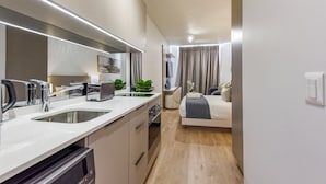 A modern kitchen with a built-in oven, a sink, and a toaster. There is a bed with a gray blanket and pillows in the adjacent room. - The Velvet Touch | One Rosebank Studio (Johannesburg)