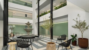 En modern, inredd entréhall med en central fontän, svarta stolar, krukväxter och ett tak med flera nivåer som är dekorerat med grönska.