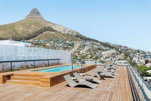 Un área de piscina en la azotea con sillones de descanso y vistas a una colina con un pico característico.