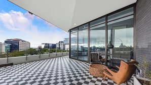 Un balcón moderno con suelo a cuadros, grandes puertas de cristal y vista panorámica de la ciudad.