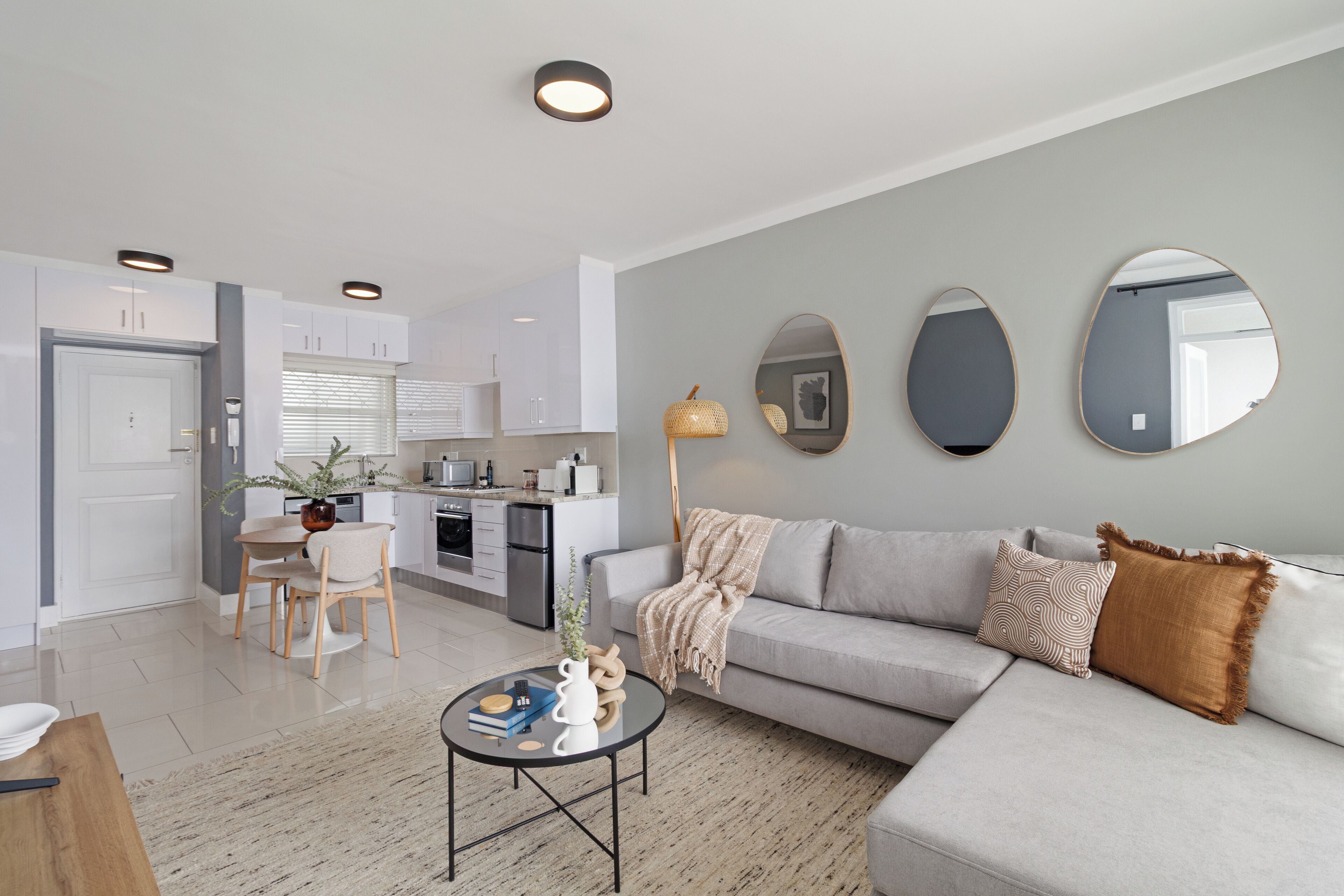 A modern living room with a grey sofa, a coffee table, and a dining area with a table and chairs.