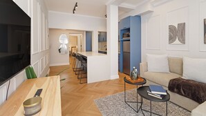 A modern living room with a flat-screen TV, a wooden coffee table, a sofa, and a small side table with books. - Modern Venetian Elegance in CBD (Cape Town)