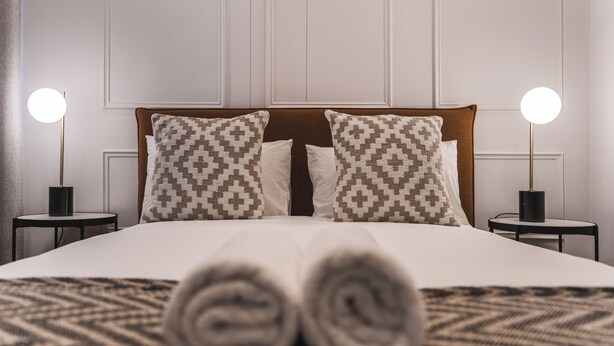 A neatly made bed with patterned pillows, two bedside lamps, and a rolled towel on the bed. - Modern Venetian Elegance in CBD (Cape Town)