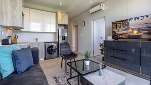 Apartamento moderno com cozinha, sala de estar e uma televisão grande exibindo uma cena de praia.