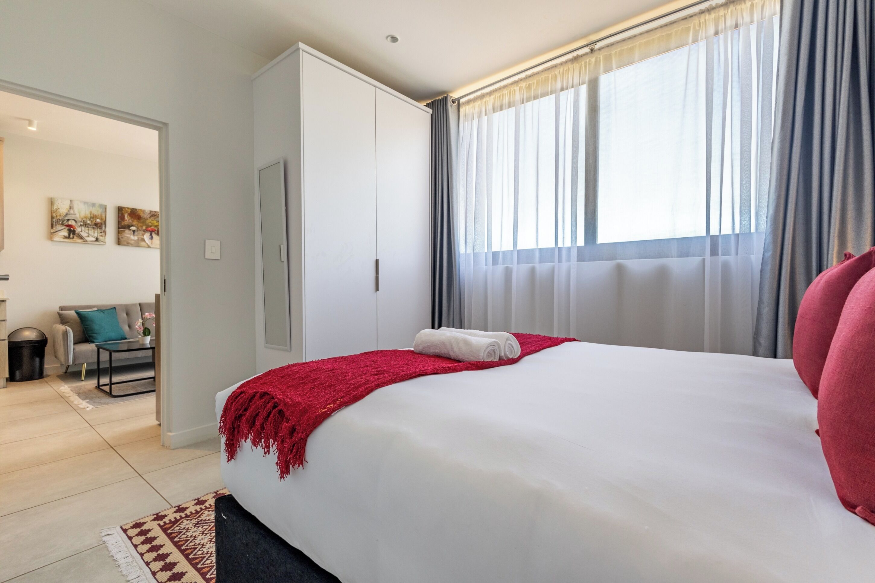 Ein Hotelzimmer mit einem großen Bett, einer roten Tagesdecke, einem weißen Kissen und einem Fenster mit Vorhängen.