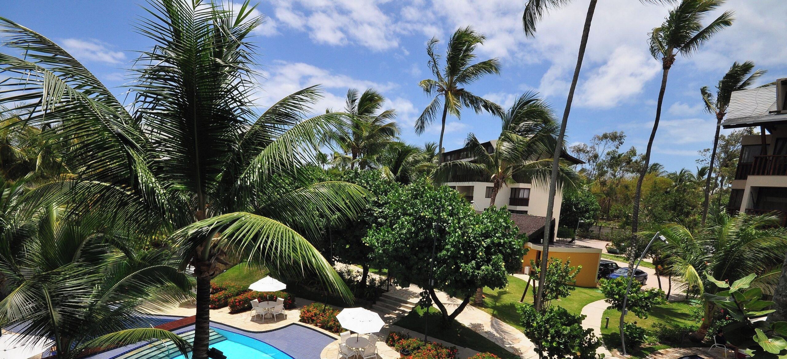 A resort with a swimming pool, palm trees, and a building with balconies.