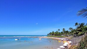 Uma praia com águas azul-claras, palmeiras e uma costa arenosa.