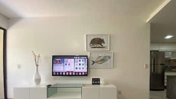 A modern living room with a flat-screen TV mounted on a white cabinet, a vase with flowers, and two framed pictures on the wall.