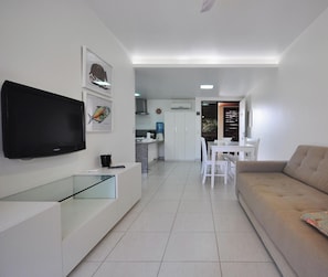 A modern living room with a flat-screen TV, a glass coffee table, a sofa, and a dining area with a white table and chairs. - Nannai Residence (Ipojuca)