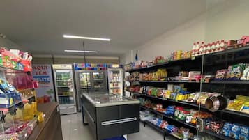 Interior de um supermercado, com seções refrigeradas, prateleiras repletas de diversos produtos e uma área de pagamento.