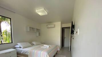 A bedroom with a bed, a bedside table, a wardrobe, and a window with a view of palm trees.