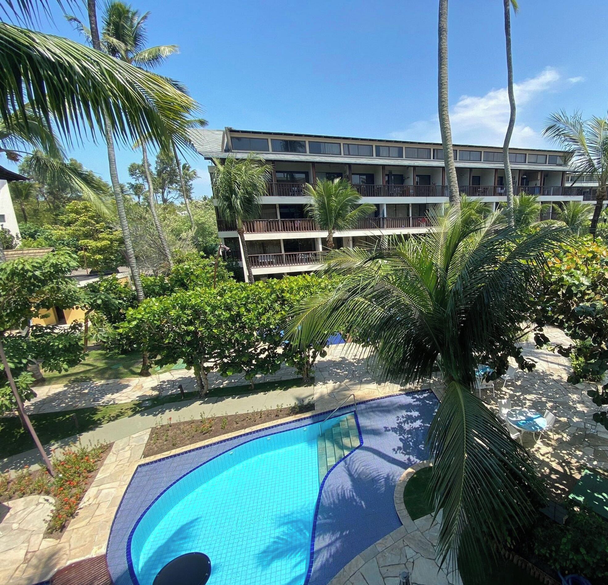 A hotel with a swimming pool surrounded by palm trees and a multi-story building in the background.