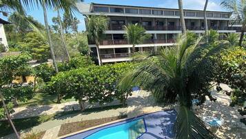 A hotel with a swimming pool surrounded by palm trees and a multi-story building in the background.
