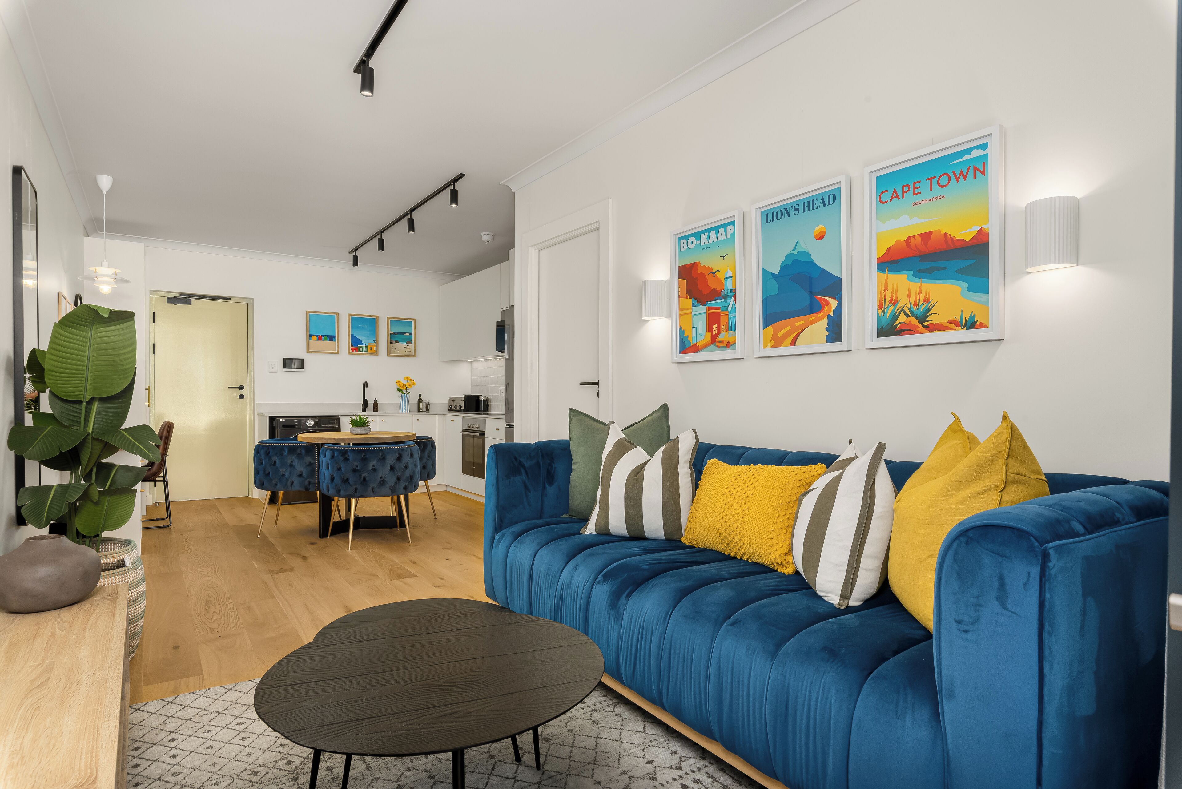 Een moderne woonkamer met een blauwe bank, een ronde salontafel en een eethoek met een blauwe stoel en een kleine tafel.