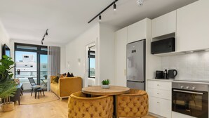 A modern kitchen with white cabinets, a built-in microwave, and a Bosch oven. There is a round wooden table with two chairs and a small plant on it. - Stylish Apartment in the Heart of Sea Point (Cape Town)