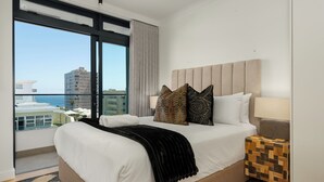 A modern hotel room with a large bed, a view of the city, and a nightstand with a lamp. - Stylish Apartment in the Heart of Sea Point (Cape Town)