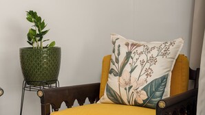 Une pièce comprenant un fauteuil en bois avec un coussin jaune, une plante verte en pot et un tableau encadré accroché au mur.