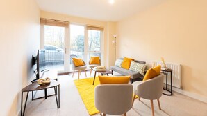 A modern living room with a sofa, two armchairs, a coffee table, and a floor lamp. Large windows provide natural light and a view of the outside. - Bright 2BR Flat • Parking • 1 Min to Tube/Metro • Next to London Museum - Pass the Keys (London)