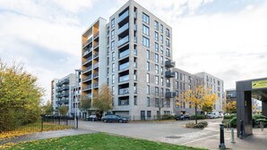 A multi-story residential building with balconies, a gated parking area, and a small park with trees. - Bright 2BR Flat • Parking • 1 Min to Tube/Metro • Next to London Museum - Pass the Keys (London)